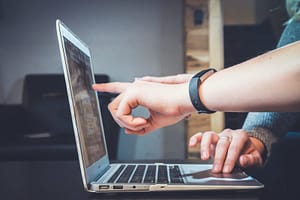 Image of a laptop with one hand pointing at screen.