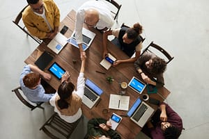 Image of team sitting at table on computers, with two people shaking hands