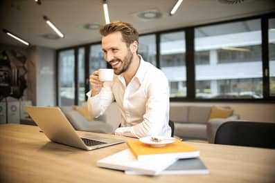 Image of man sipping coffee in front of laptop 